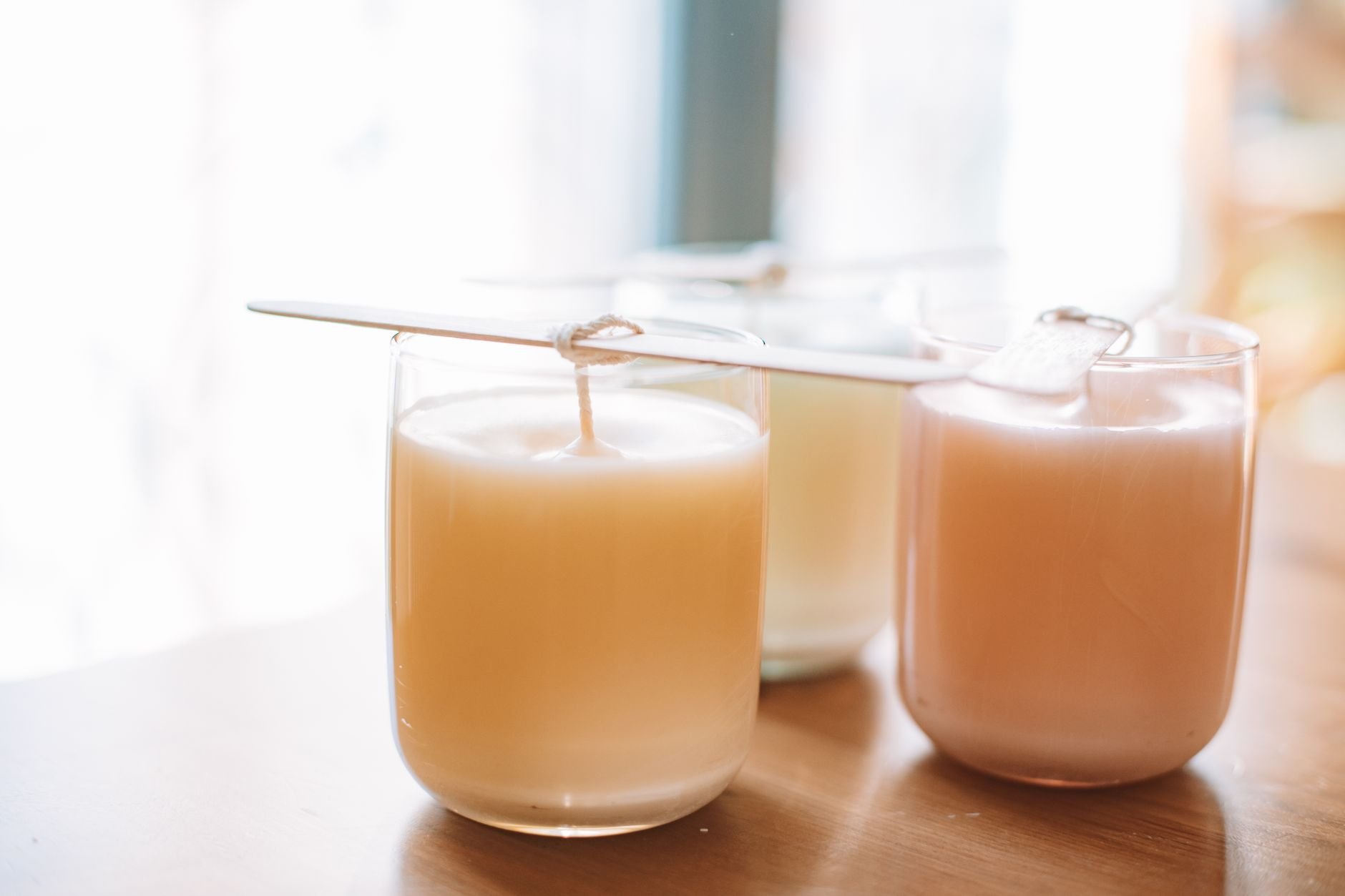 A still life of handmade candles in glass jars with wicks, captured in warm natural light.